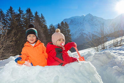 Portrait of smiling couple sitting on snow covered mountain