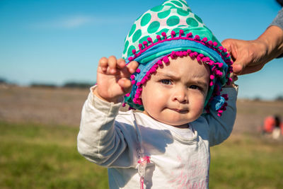 Cropped hand of woman holding baby hat on grass against sky