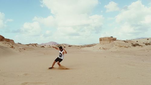 Full length of young man standing on sand at beach against sky