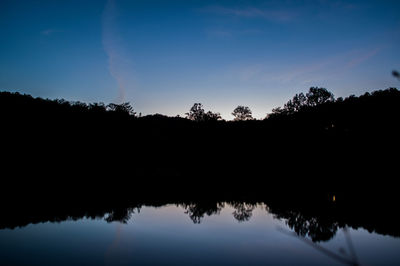 Silhouette trees by lake against sky during sunset