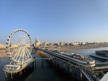 Ferris wheel by river against clear blue sky