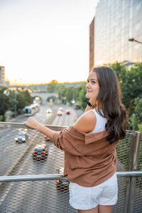 Side view of young woman standing against railing