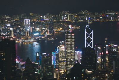 Illuminated cityscape by river against sky at night