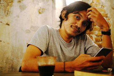 Portrait of young man using mobile phone while sitting on table