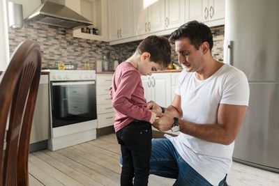 Father dressing up son while kneeling on kitchen floor