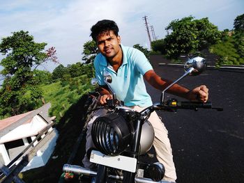 Side view of young man riding motorcycle against trees