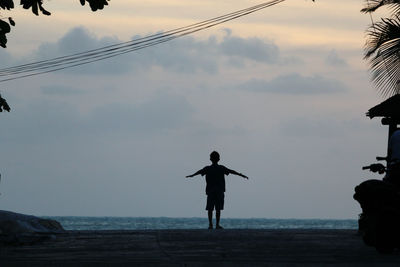 Silhouette boy standing at beach against sky during sunset