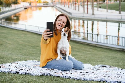 Young caucasian woman woman taking picture with mobile phone. woman having fun with jack russell dog