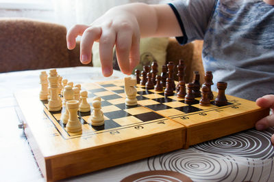 Midsection of child playing chess on table at home