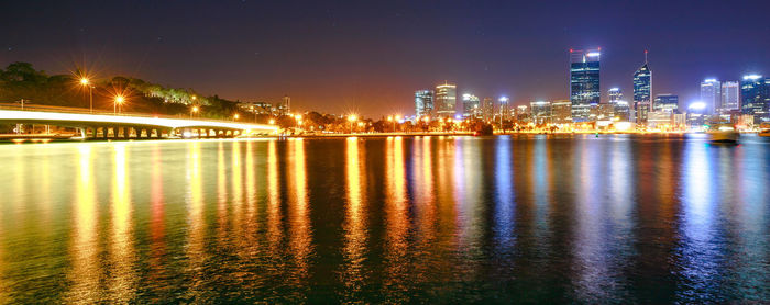 Illuminated buildings by river against sky at night