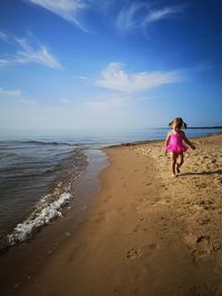 Girl walking on shore at beach against sky