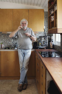 Full length of senior man drinking coffee while standing at kitchen