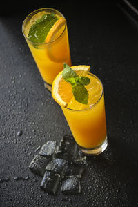 Top view of glasses of orange juice with melting ice on black surface