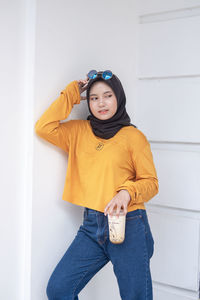 Portrait of young woman standing against wall