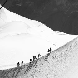 Low angle view of people walking on snowcapped mountain during sunny day