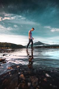 Full length side view of man standing on stones in sea