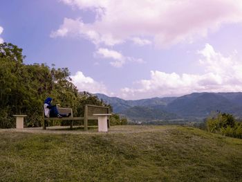 Man sitting on field against sky