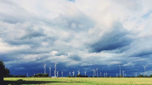 Wind turbines on field against cloudy sky