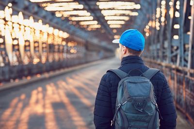 Rear view of young man walking on bridge during sunset