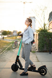 Young woman standing on push scooter against sky