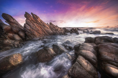 Rocks in sea against sky during sunset