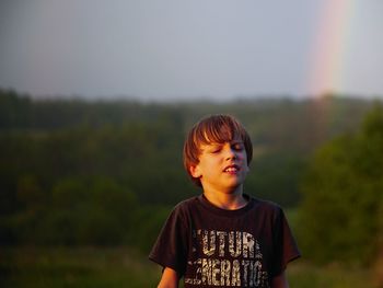 Boy with eyes closed standing against trees during sunset