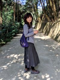 Portrait of woman standing on footpath against trees