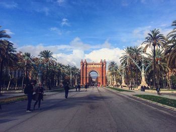 People on road leading towards gate against sky