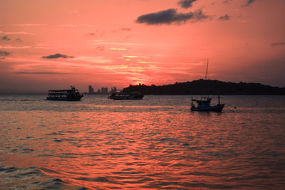 Silhouette boat sailing on sea against orange sky