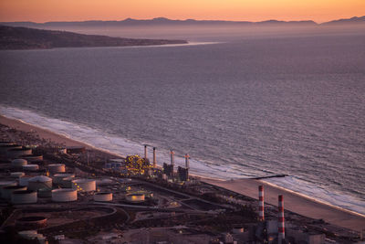 High angle view of industrial buildings by sea during sunset