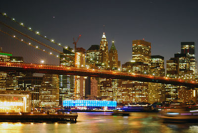 Illuminated bridge over river by buildings against sky at night