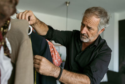 Mature male tailor measuring clothes on coathanger at work studio
