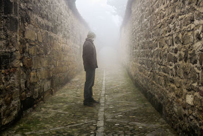 Rear view of man walking on footpath amidst wall