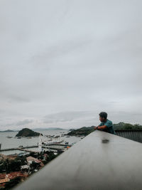 Rear view of man standing on shore against sky