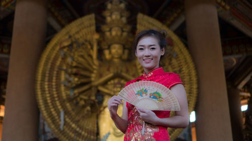 Portrait of smiling young woman holding hand fan outside temple