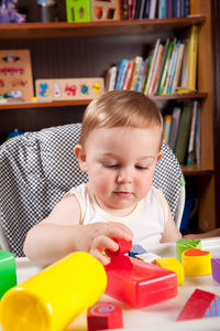 Cute baby boy playing with toys on table at home