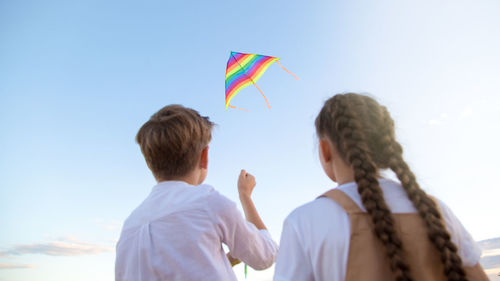 A girl and a boy launch bright kite into the sky, a view from the back.