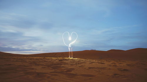 Heart shape on sand dune against sky