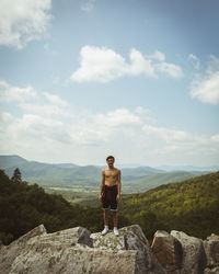 Shirtless man standing on rock against mountains