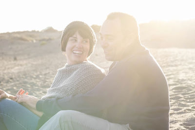 Smiling couple embracing while sitting at beach