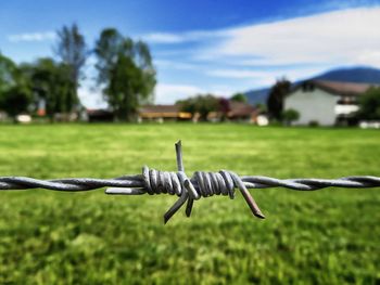 Close-up of barbed wire fence on field against sky