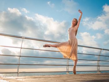 Mid adult woman standing by railing against cloudy sky during sunset