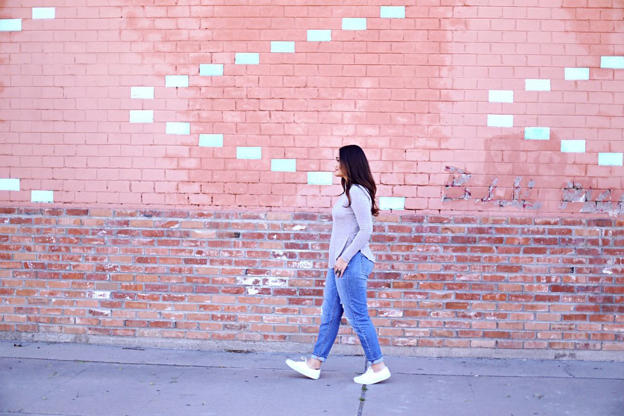 full length, brick wall, casual clothing, building exterior, lifestyles, architecture, built structure, standing, wall - building feature, walking, rear view, leisure activity, young adult, young women, side view, front view, street, person