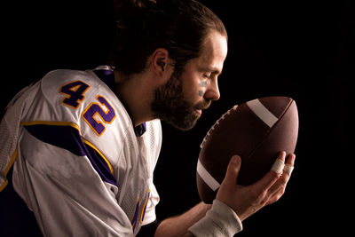 Portrait of young man holding ball against black background