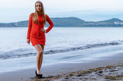Full length portrait of smiling young woman on beach against sky
