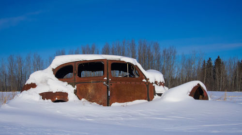 A snow covered, antique car slowly rusts away