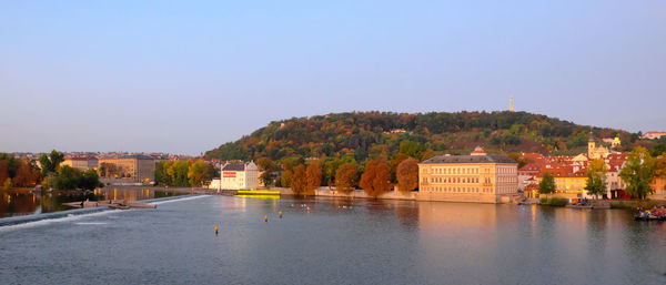 Buildings by river against clear blue sky