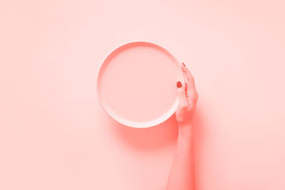 Close-up of hand holding drink against pink background