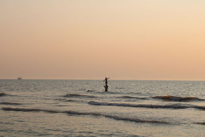Silhouette person in sea against sky during sunset