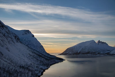 Scenic view of sea by snowcapped mountains against sky during sunset